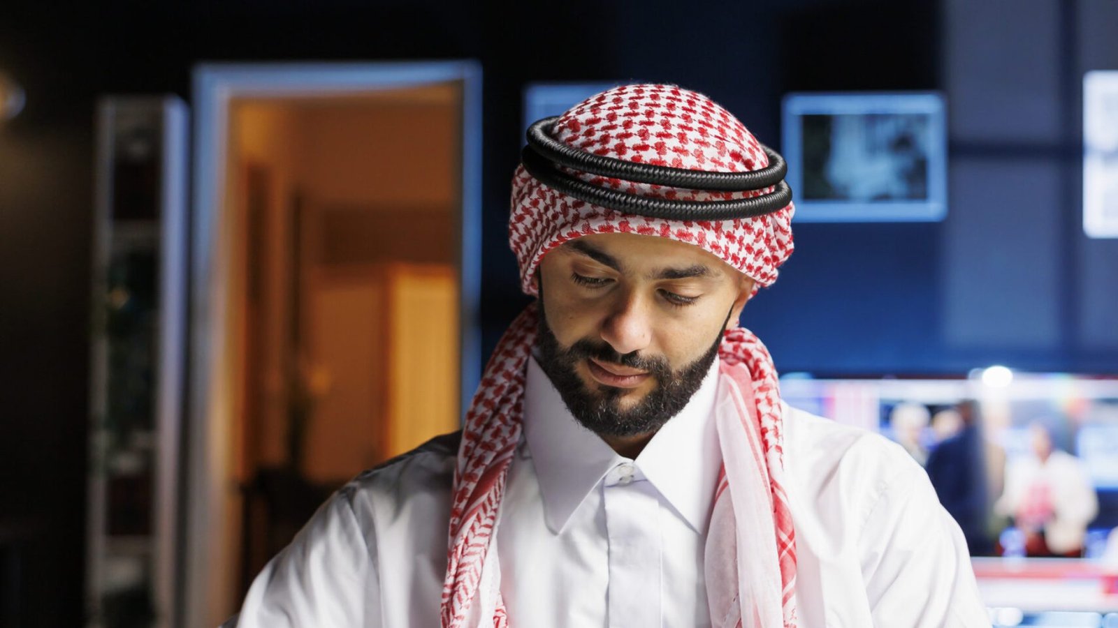 Professional Muslim guy uses technology to work efficiently in the office, browsing online and writing notes from a laptop. Youthful Arab male student using his notebook and minicomputer for research.